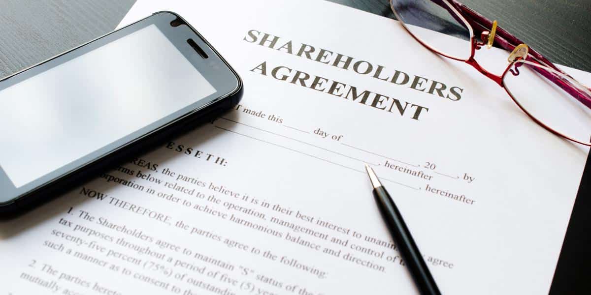 a piece of paper that says "shareholder's agreement" with a phone, pen and glasses next to it.